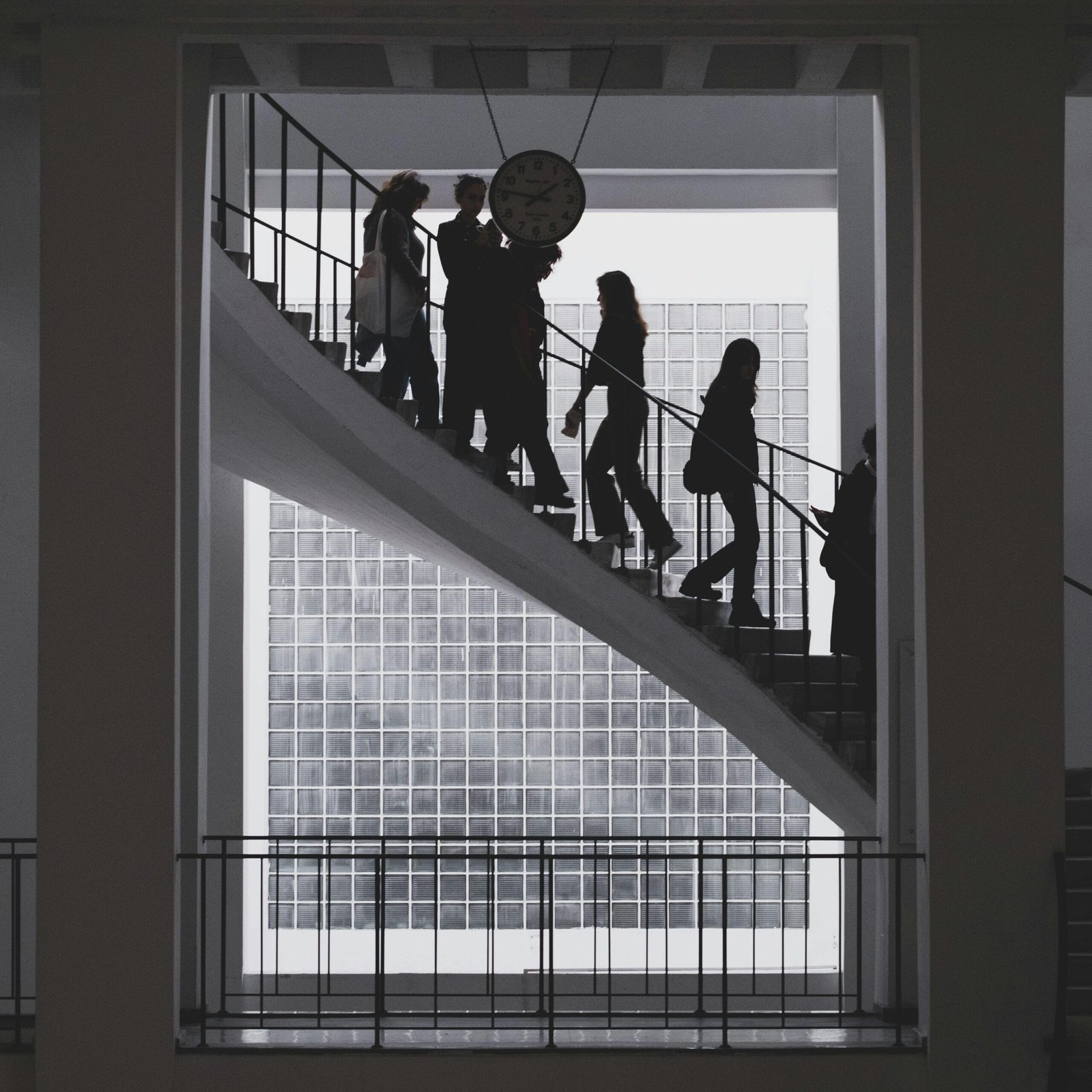 Silhouetted people ascending a modern staircase in a bright office building.