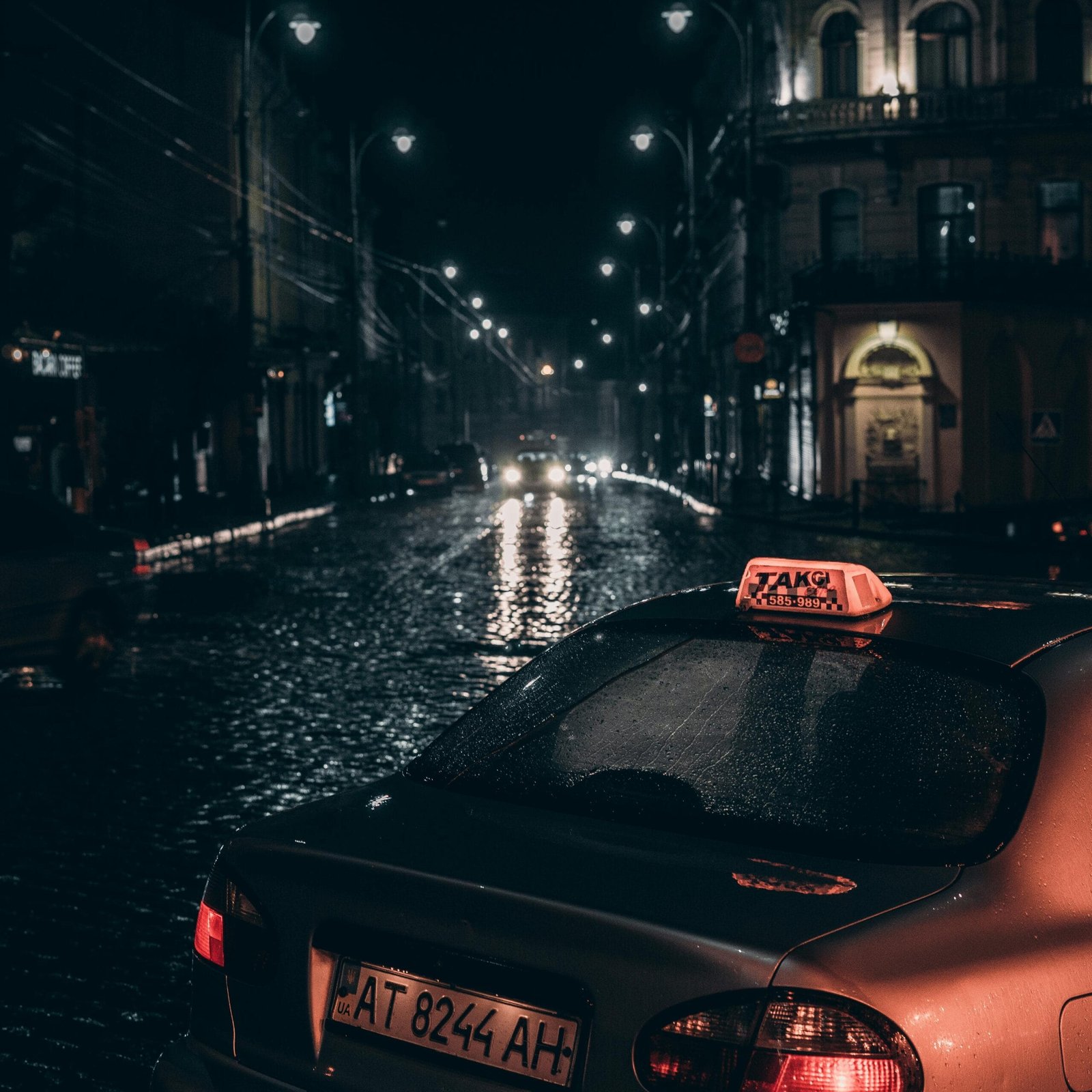 Dramatic city street scene with a taxi and rain-soaked cobblestones at night.