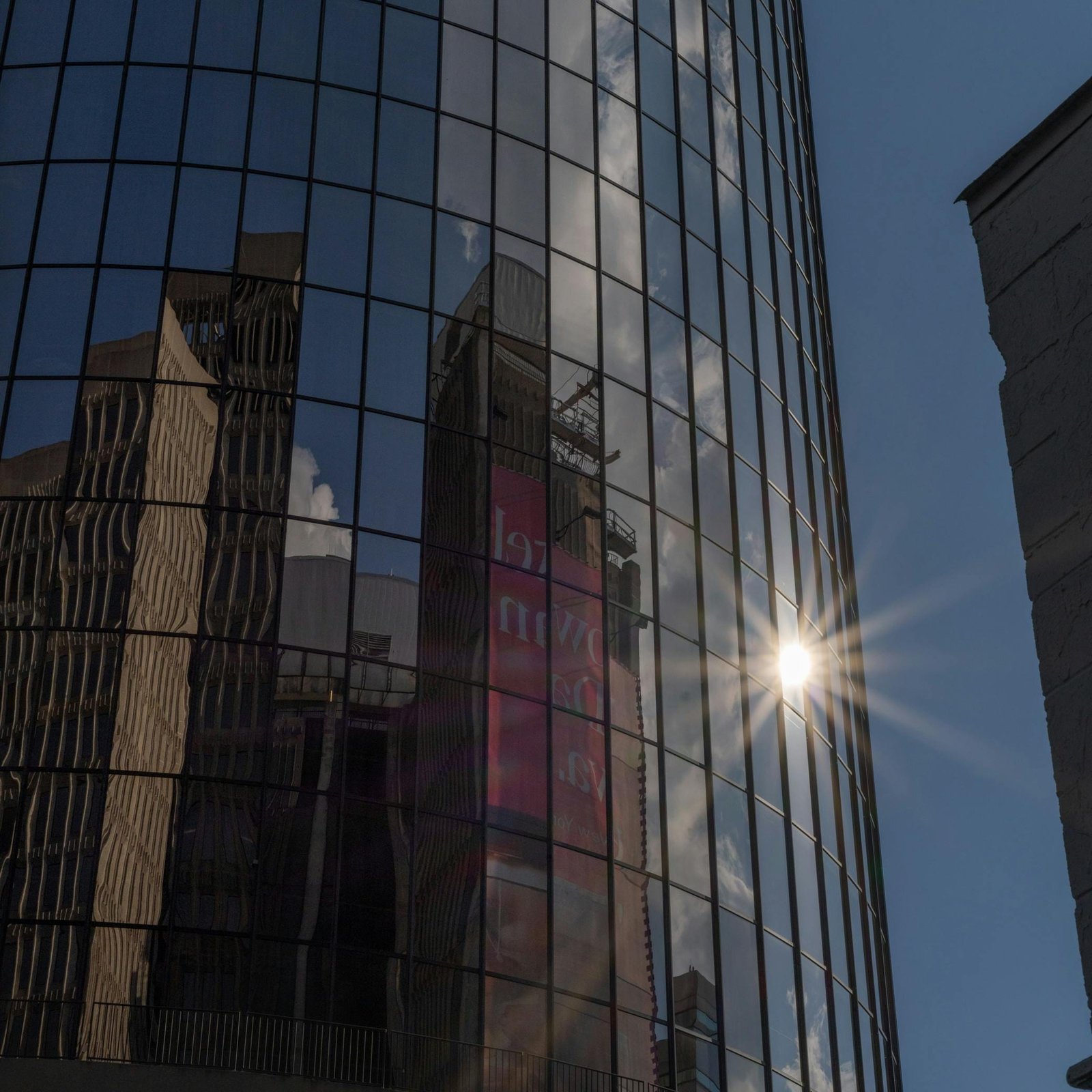 Glass skyscraper reflecting cityscape with sunburst in urban setting.