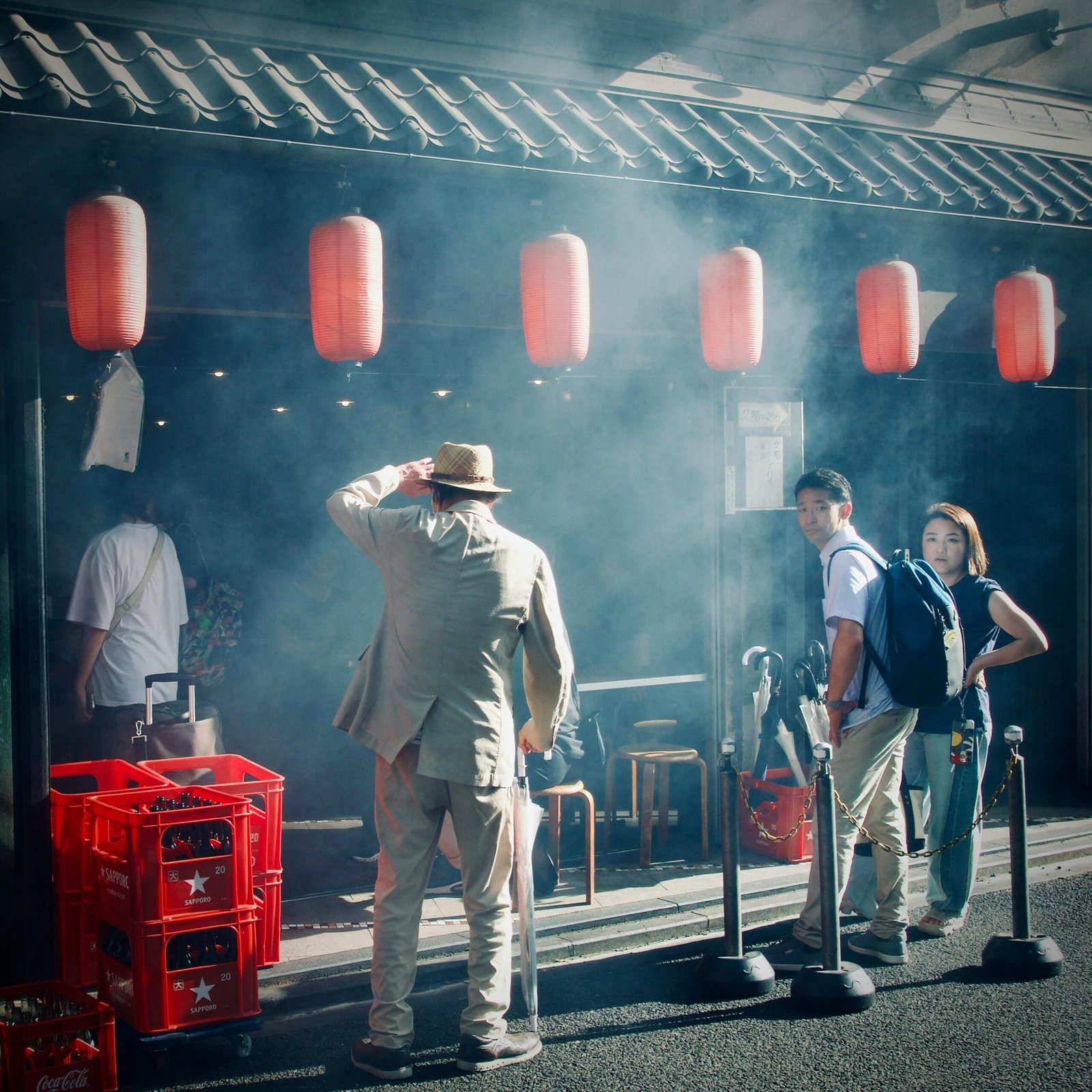 A bustling street scene outside a Japanese izakaya with red lanterns and waiting patrons.