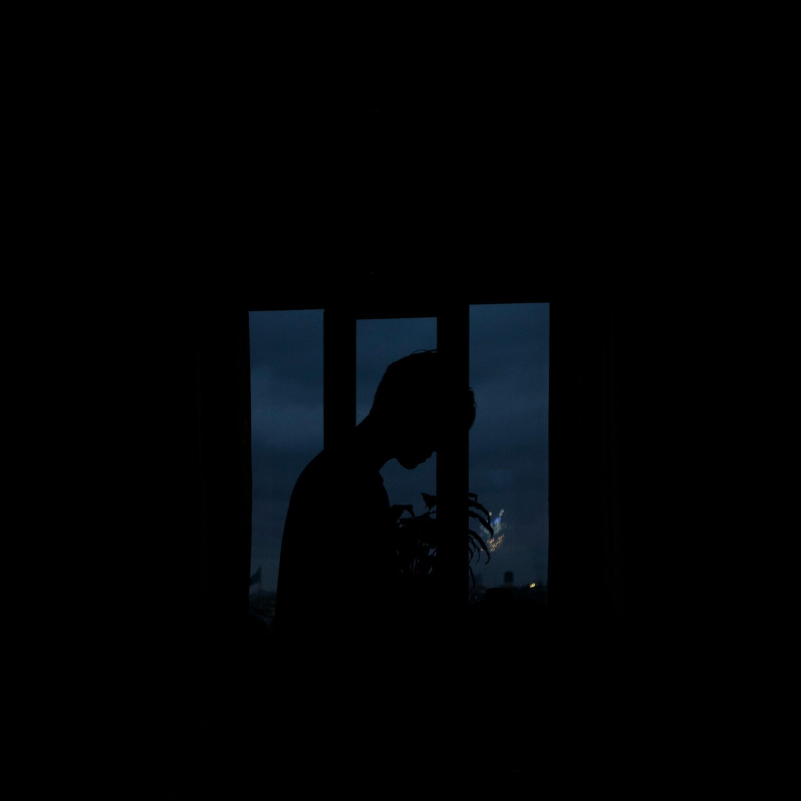 Moody silhouette of a person framed by a window with a dark, twilight sky in the background.