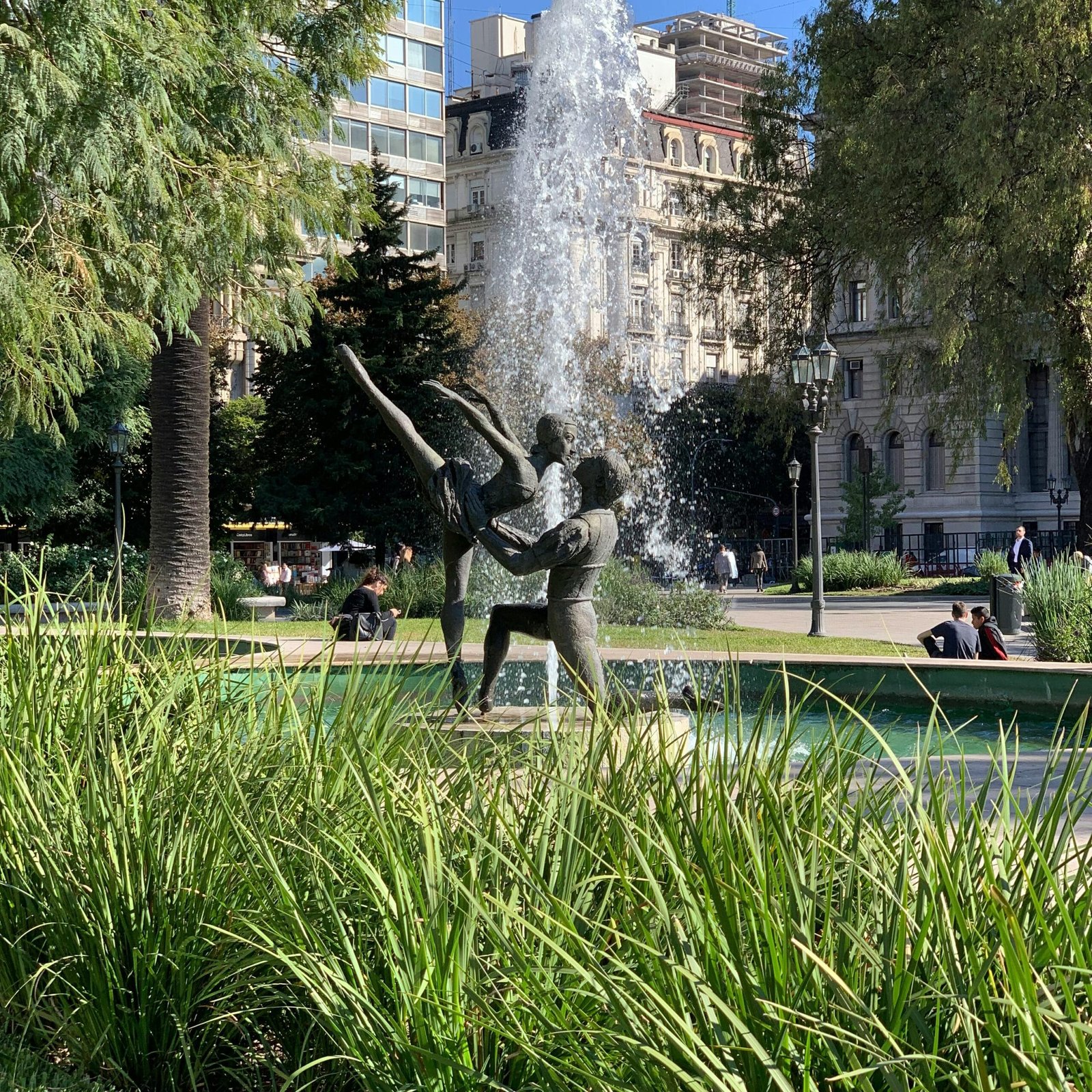 Statue of dancers in a Buenos Aires park fountain with surrounding greenery.