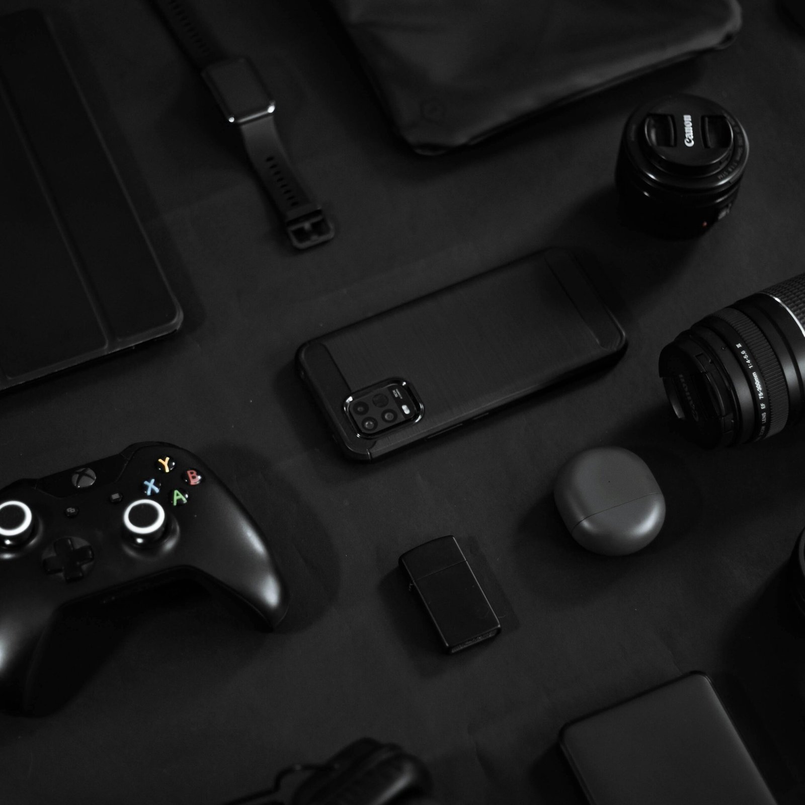 Stylish arrangement of gadgets including a smartphone, lens, and game controller on a black surface.