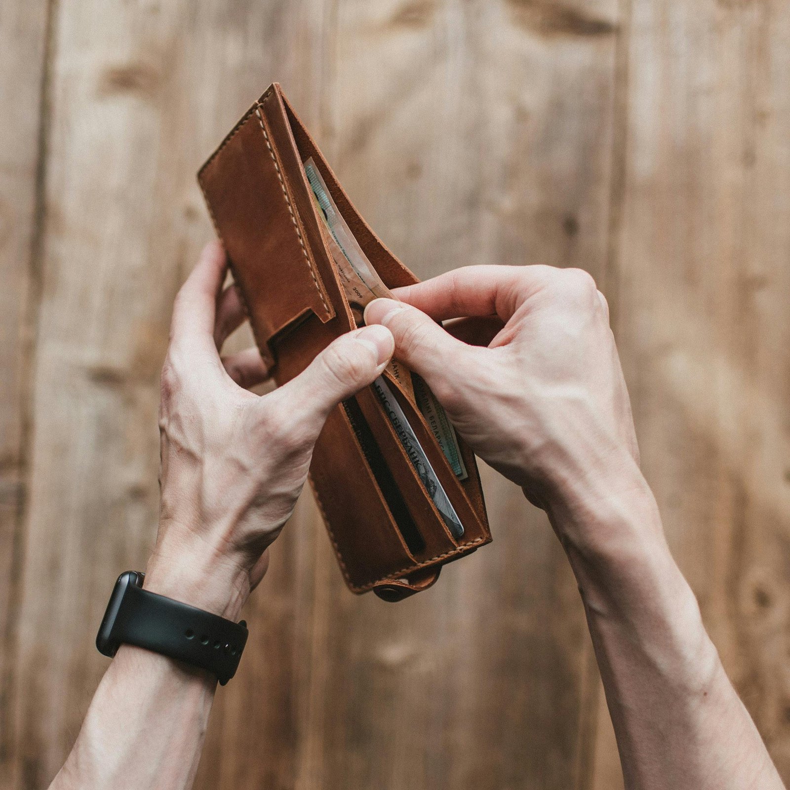 Close-up of hands holding a leather wallet with cash on a wooden background.
