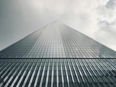 A dramatic low angle shot of One World Trade Center against cloudy skies in New York City.