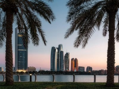 Beautiful Abu Dhabi cityscape at dusk with skyscrapers framed by palm trees and a tranquil water view.