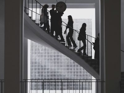 Silhouetted people ascending a modern staircase in a bright office building.