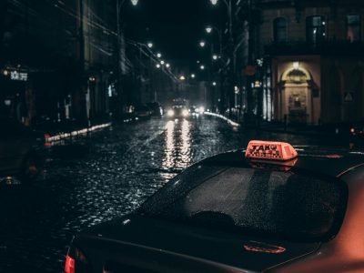 Dramatic city street scene with a taxi and rain-soaked cobblestones at night.