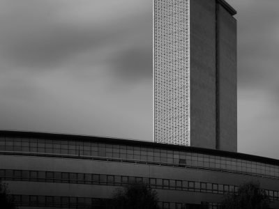 Grayscale photo of a modern skyscraper against a cloudy sky in an urban setting.