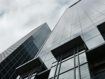 Low angle view of two modern skyscrapers with glass facades against a cloudy sky.