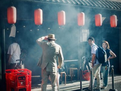 A bustling street scene outside a Japanese izakaya with red lanterns and waiting patrons.