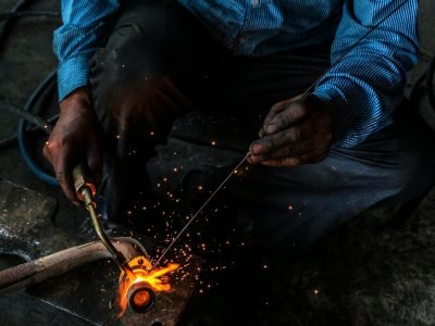 From above of crop unrecognizable workman using welding machine with gas flame while working with metal pipe