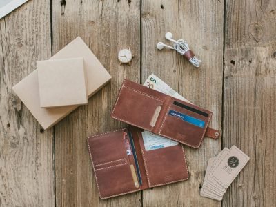 Brown leather wallet with cash, cards, and a watch on a rustic wooden background.