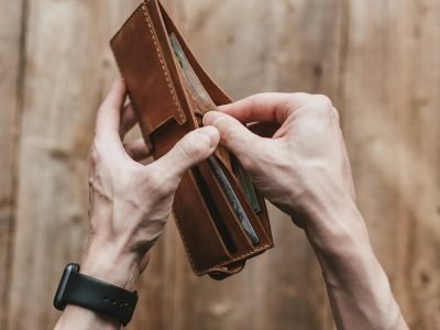 Close-up of hands holding a leather wallet with cash on a wooden background.