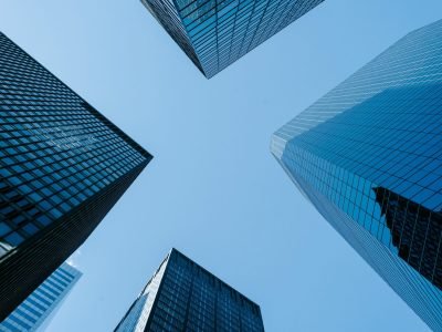 Low angle of high business towers with glass mirrored windows located in megalopolis downtown against blue sky