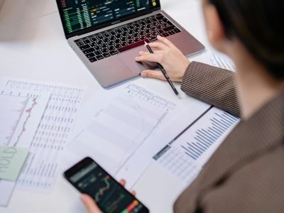 A business professional analyzing stock charts on a laptop and smartphone at the office.