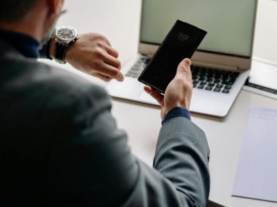 Man in office using smartphone and laptop, showing time management.