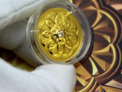 A gloved hand holds a decorative gold coin in a protective casing, showcasing intricate designs.