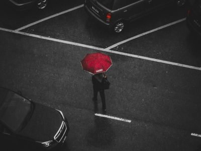 Top view of a person with a red umbrella walking in a rainy parking lot.